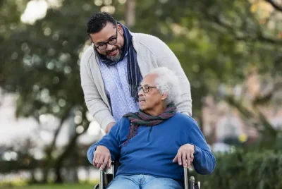 Caregiver pushing old man in a wheelchair outside